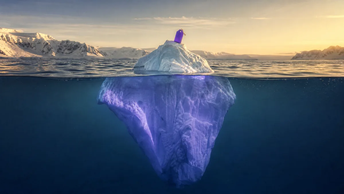 Photoreal editorial hero: an iceberg at golden hour, a small purple price tag on the visible tip above the waterline and the vast mass hidden below.
